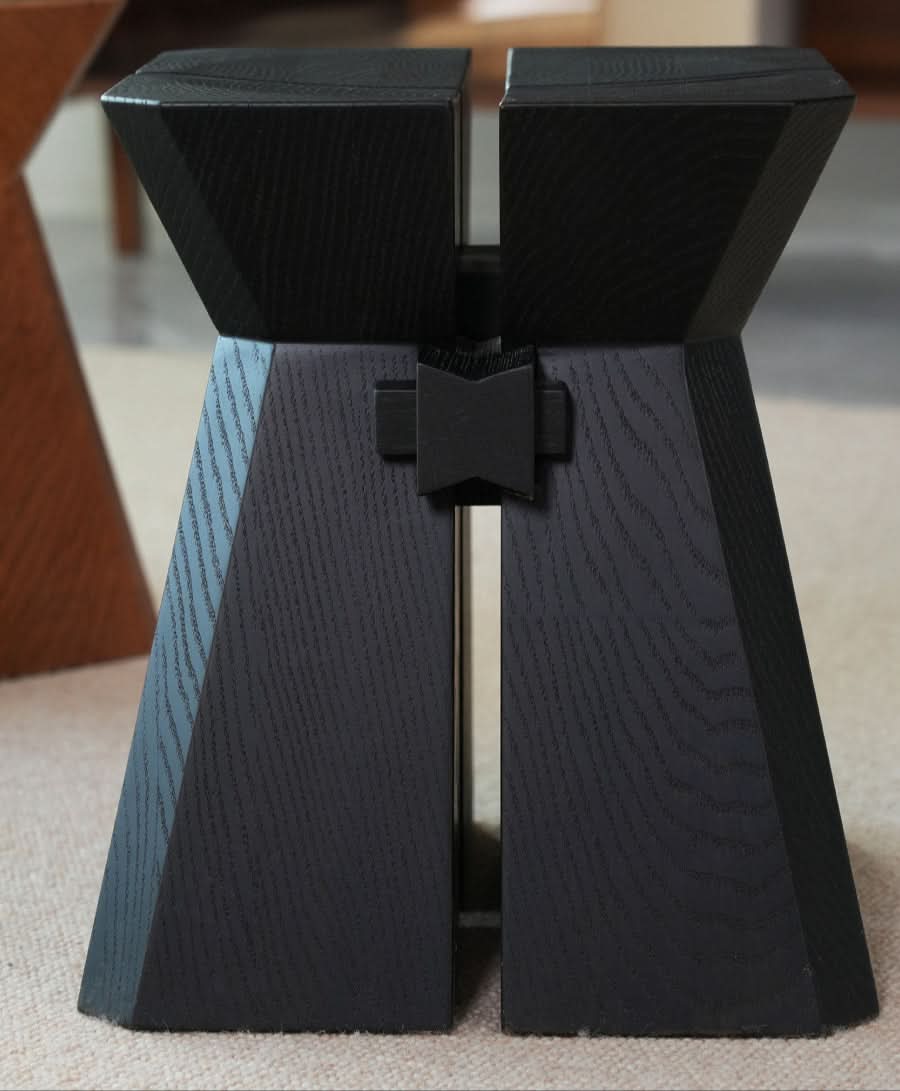 Black modern geometric wooden stool with textured wood grain on a neutral rug.